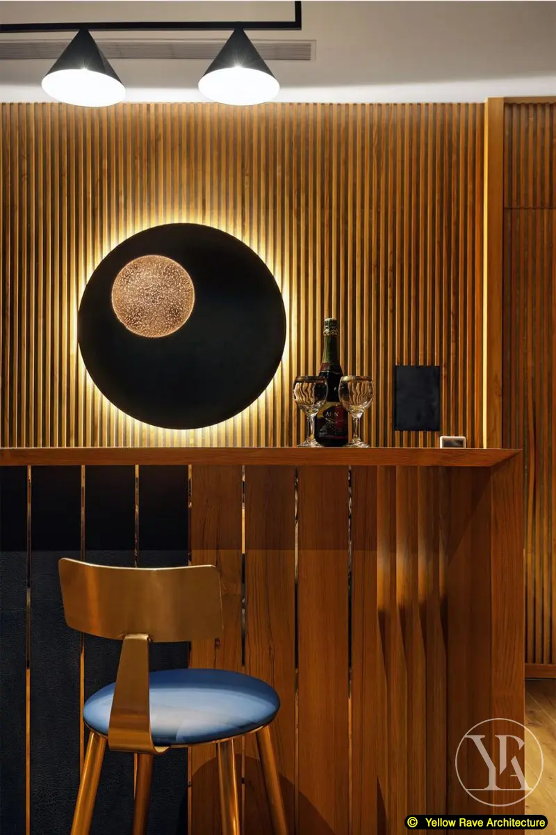 Woody Home Cinema — close-up of bar counter showing timber top, backlit black disc panel, bottle on counter and single bar stool with blue seat