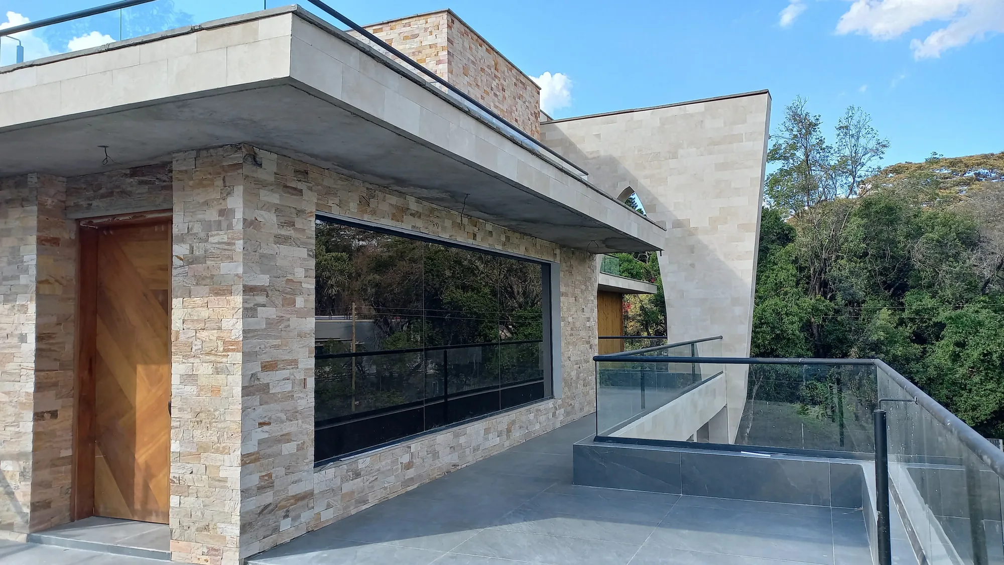 House of Wood and Marble — stone-clad screen wall with large almond-shaped open aperture cut through it, mid-construction, Runda, Nairobi