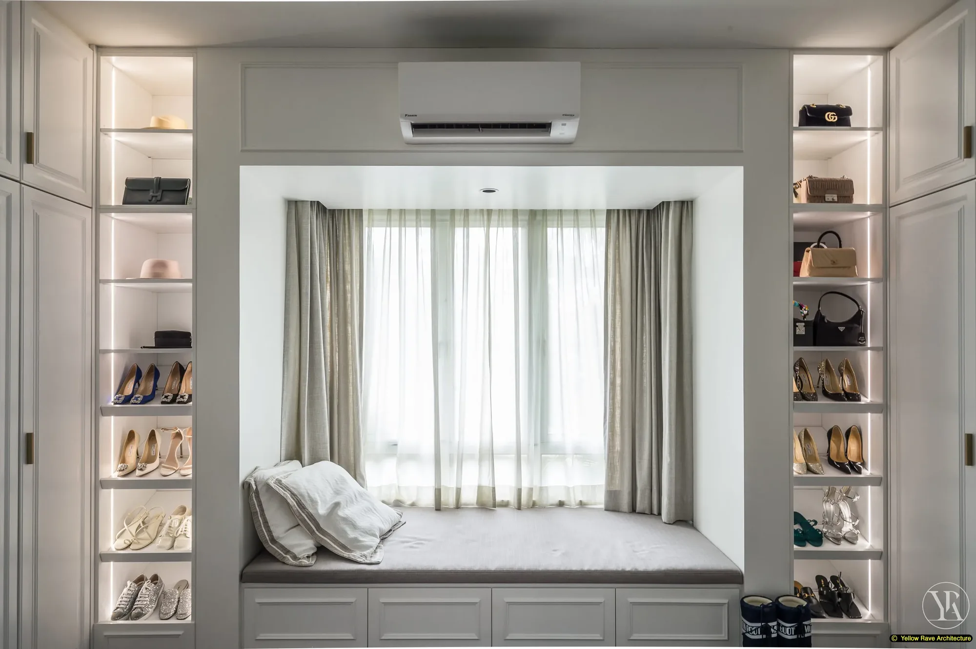 Pristine Walk-in Closet — window seat alcove with built-in cushioned bench, open LED-lit display shelving on both sides showing shoes and handbags, view to garden beyond