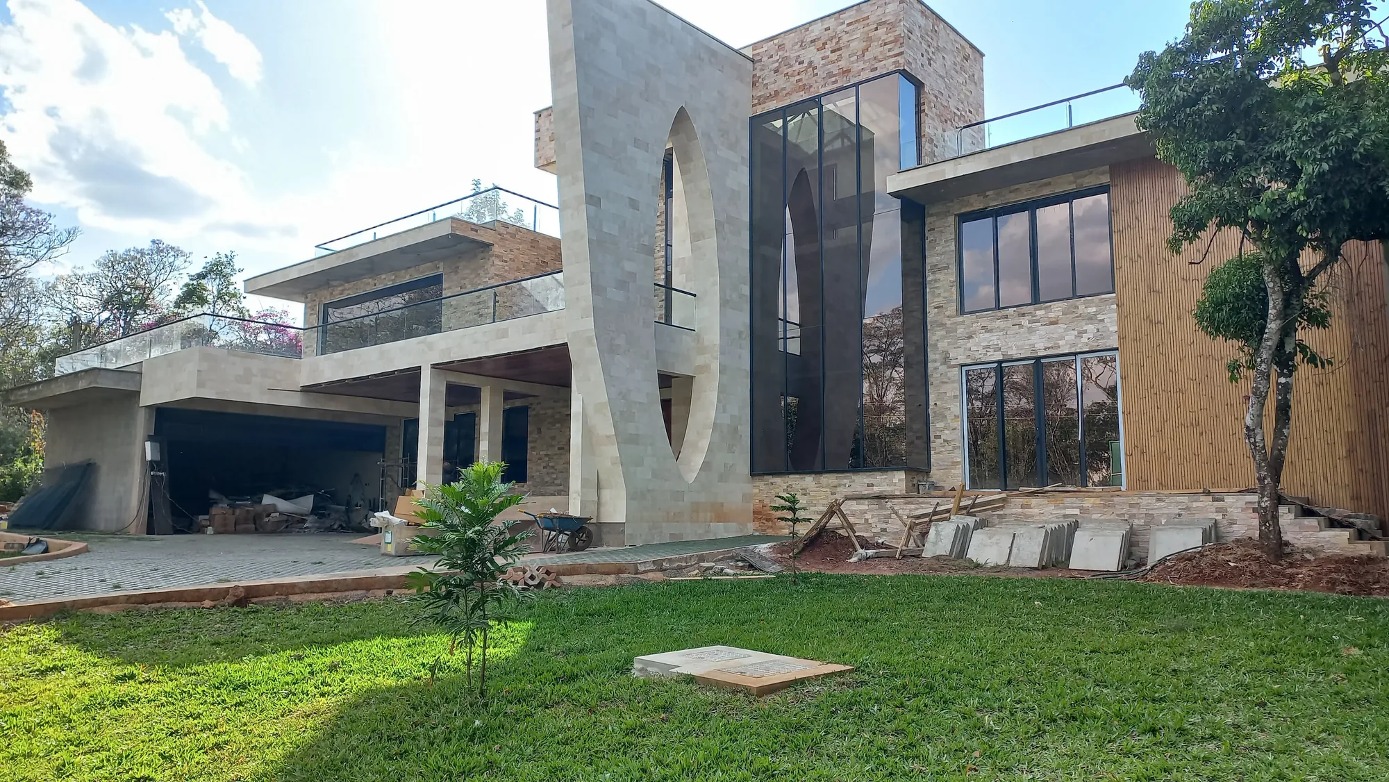 House of Wood and Marble — upper balcony under construction showing black-framed glazing, dark slate tile floor and timber slatted soffit