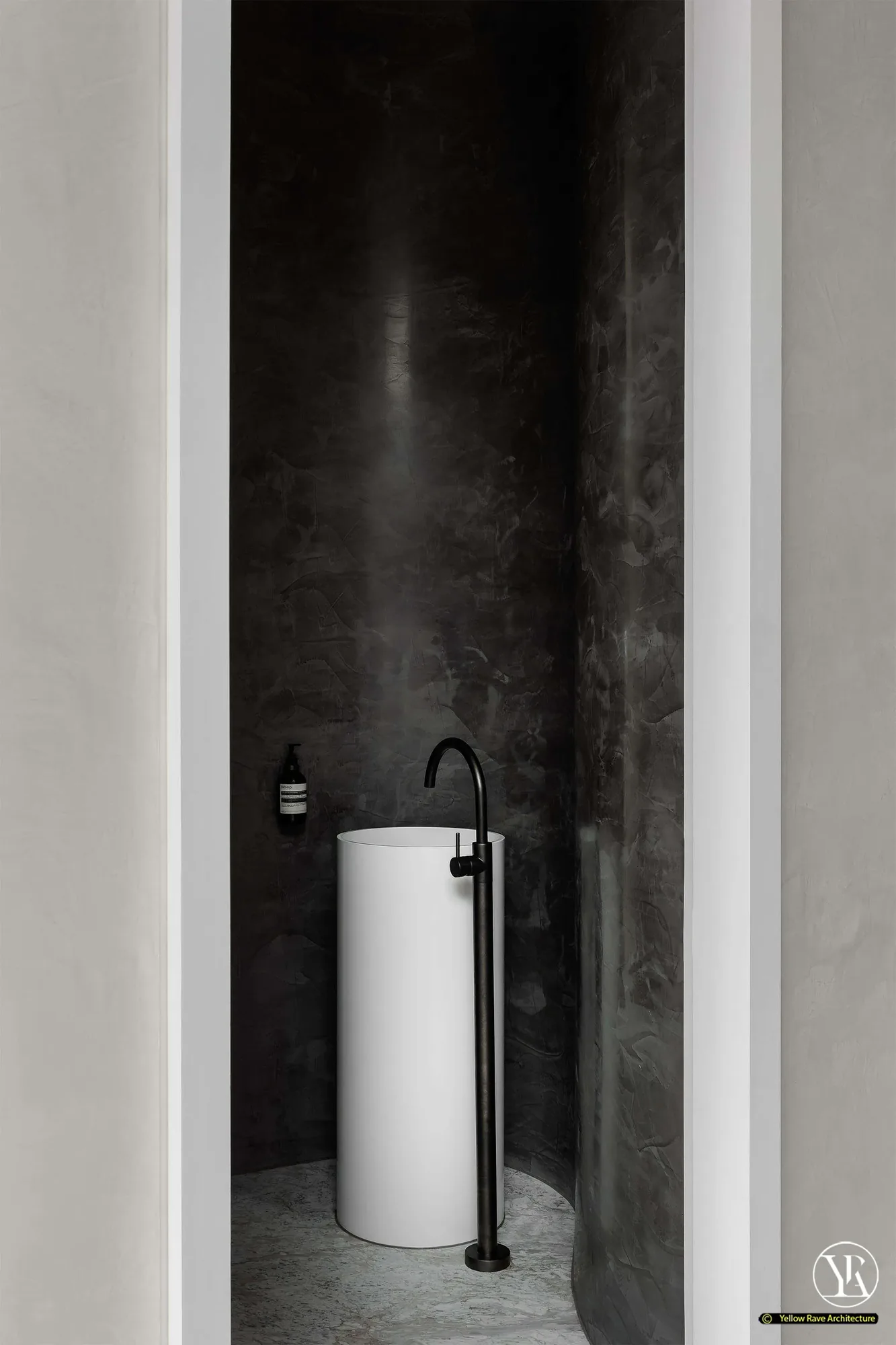 House of Privacy Walls — cloakroom WC with dark charcoal polished plaster walls, white cylindrical pedestal basin and matte black floor tap