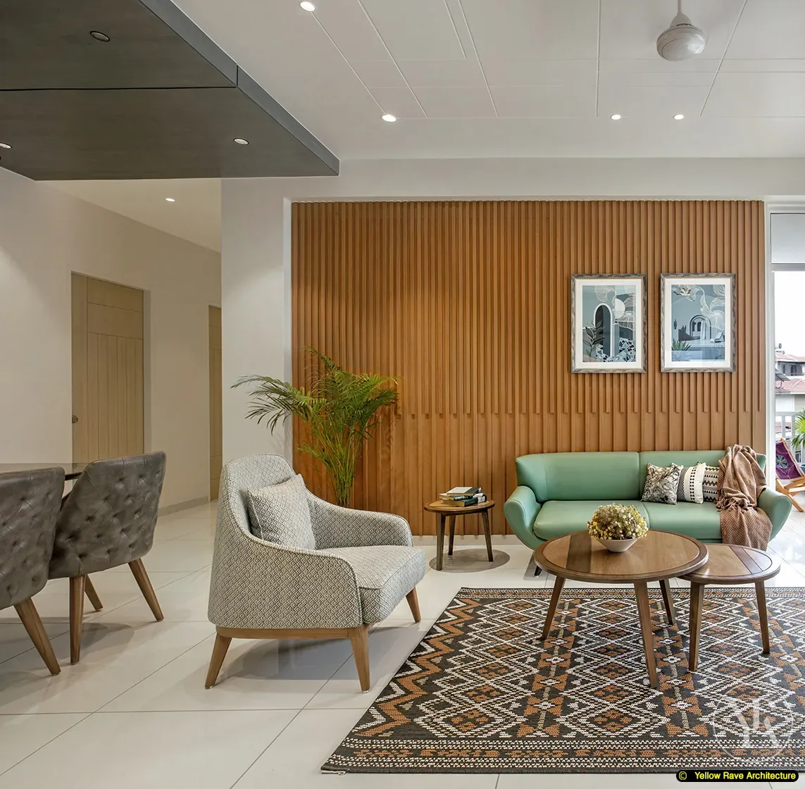 Nyali Apartment — timber batten TV wall with wall-mounted screen and floating stone-top media unit, round gold-framed mirror in entry recess to the right