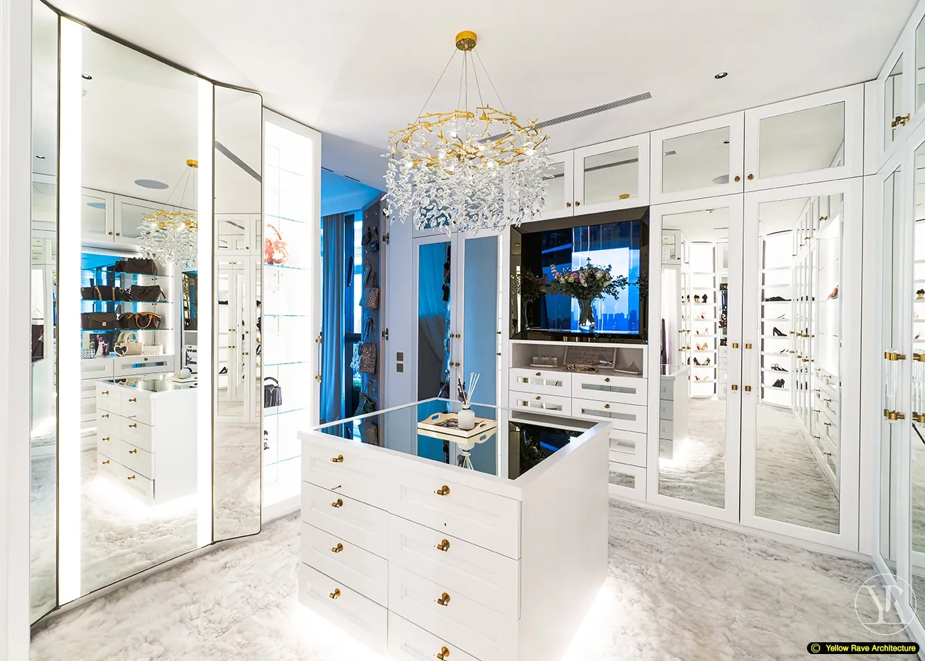 Show-Piece Wardrobe — wide interior view showing full run of white mirrored cabinet doors with gold handles, open shoe shelving, central island and gold chandelier above