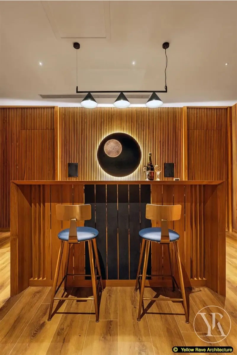 Woody Home Cinema — bar counter at rear with two timber bar stools, circular black wall sconce and backlit black disc panel above, timber batten walls throughout