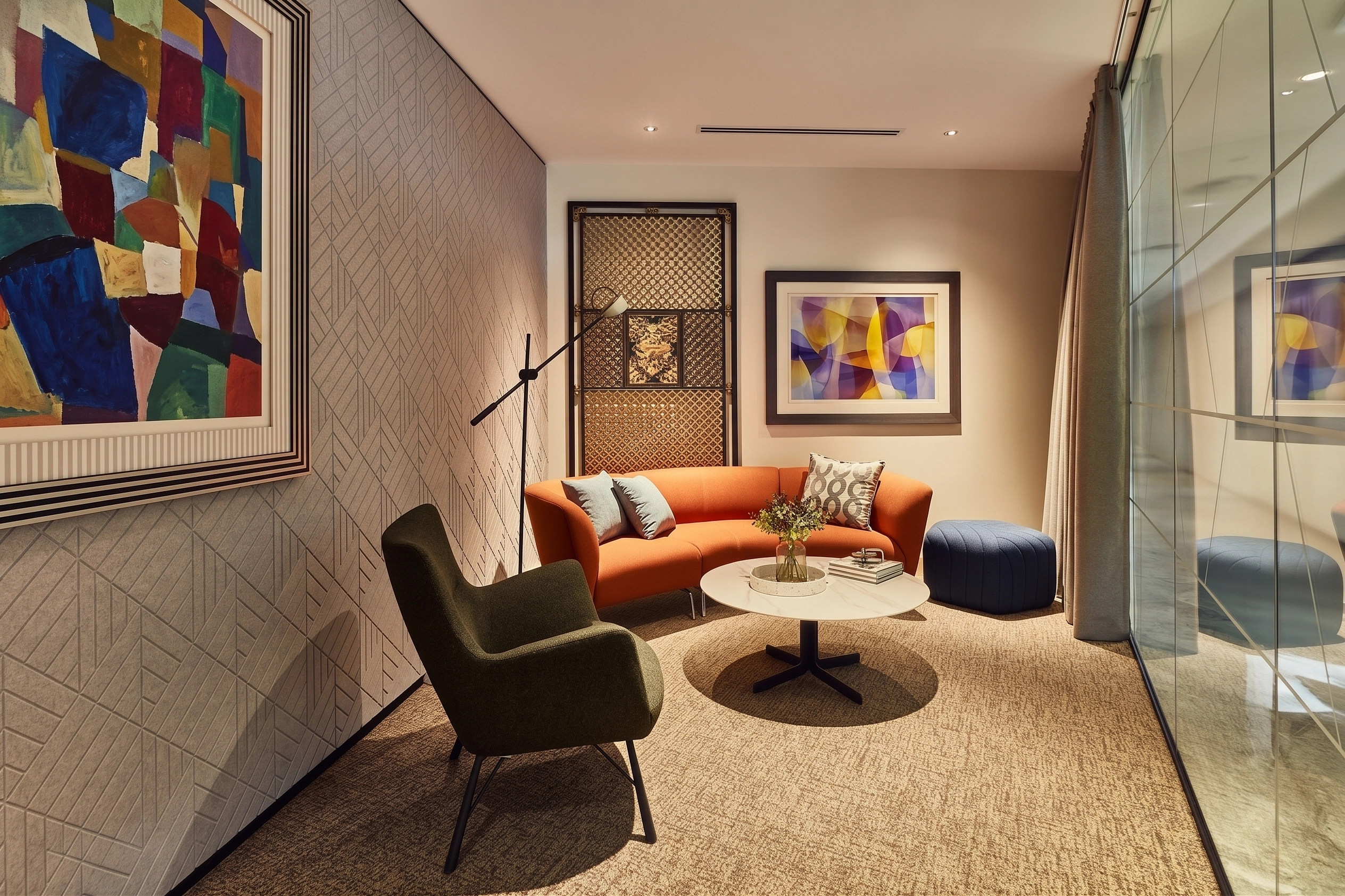 Small lounge with an orange curved sofa, green armchair, framed artwork, and a textured wall panel